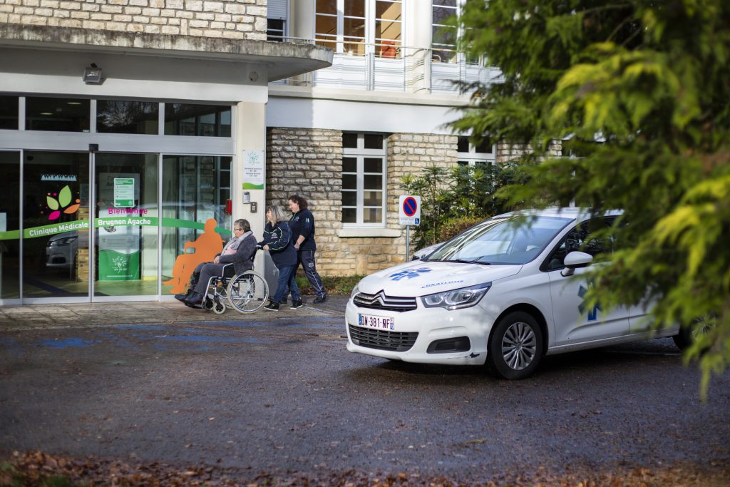 Une patiente en fauteuil roulant accompagnée de deux personnes du service de taxi médical (VSL) s'appretent à rentrer à la Clinique Médicale Brugnon Agache.